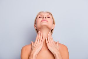 Descubra o porquê o pescoço é uma região erógena! Conheça o papel a de fatores biológicos que contribuem para isso. Venha conferir. - Retrato de uma mulher bonita, charmosa e atraente, desfrutando de sua pele perfeita, segurando as duas mãos no pescoço, com a cabeça erguida, costas com os olhos fechados, isolado em fundo cinza, hidratação, conceito de hidratação