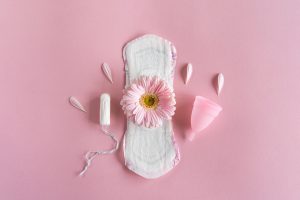 Descubra a importância de cuidar da higiene durante a menstruação e saiba se é necessário adotar uma abordagem diferente nesse período! - Conceito de período menstrual. Absorvente higiênico branco, coletor menstrual e tampão com flores cor-de-rosa. Menstruação, proteção. Saúde da mulher.